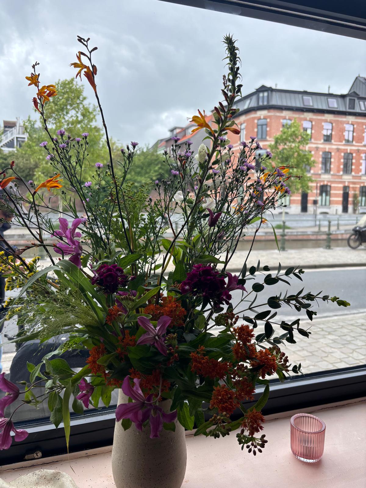 Vaas met crocosmia, asters en clematis op een vensterbank met zicht op de straat