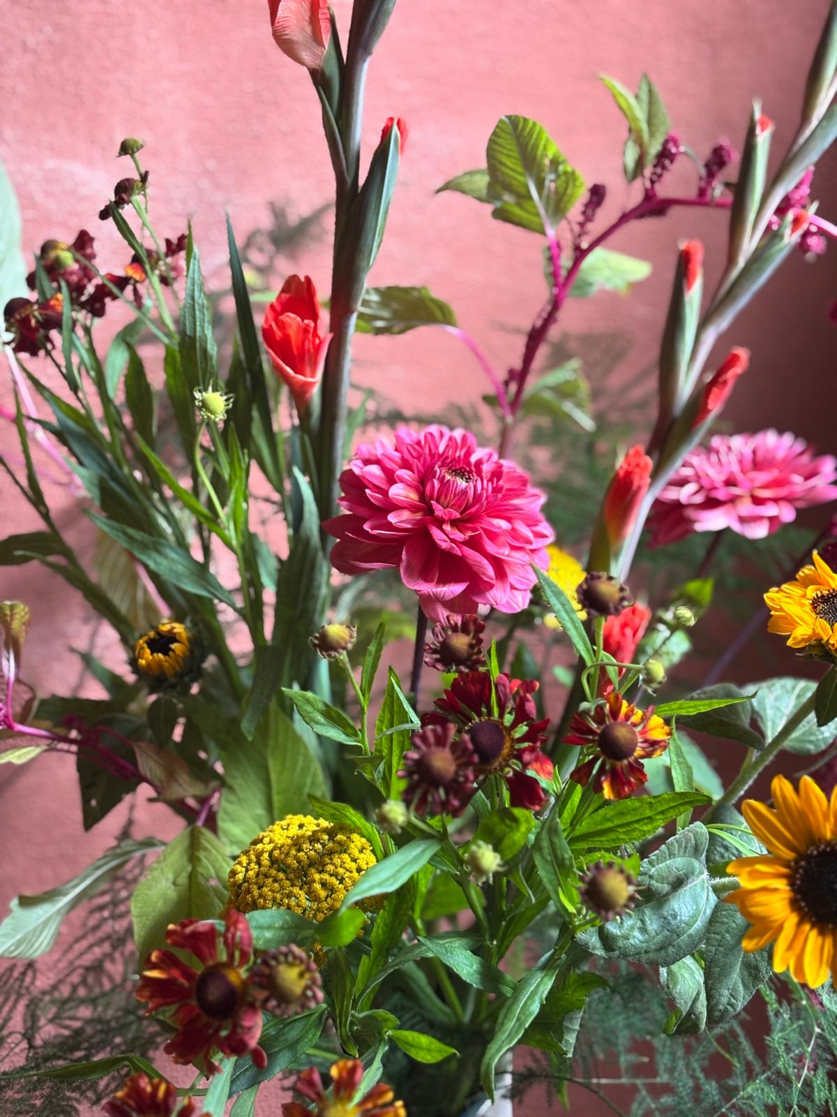 Roze dahlia's, gladiolen en zonnebloemen tegen een roze muur