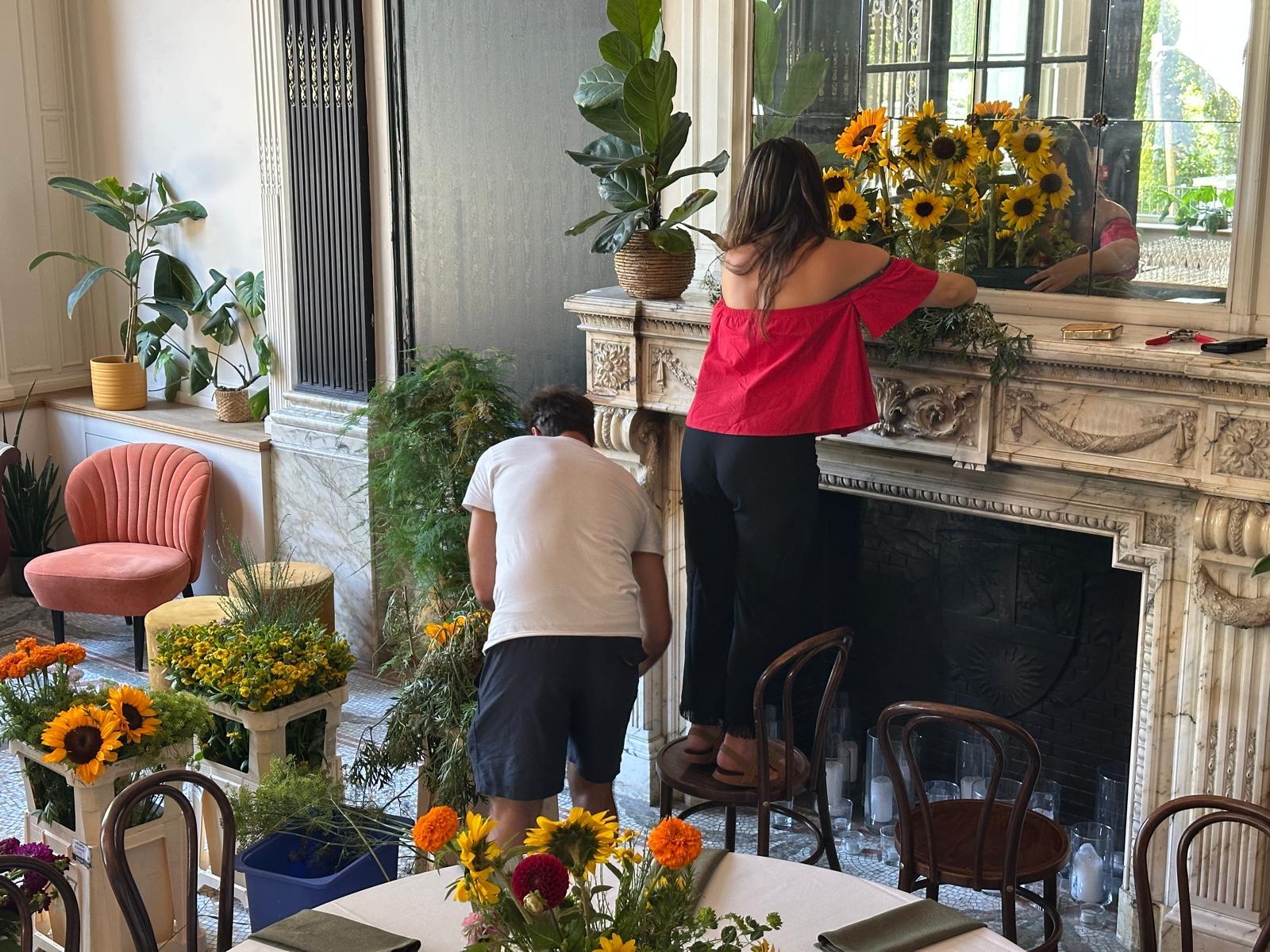 Het team bouwt de bloemen op in de zaal, met emmers vol zonnebloemen en dahlia's